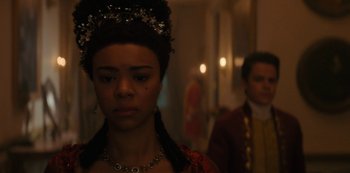 A woman wearing a crown and a necklace in front of a man in a suit