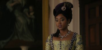 Movie still from “Queen Charlotte: A Bridgerton Story” (2023), directed by Tom Verica – A woman in a purple hat and a yellow and blue dress; Close Up shot, Over the shoulder angle