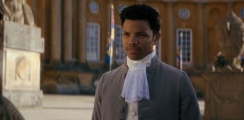 Movie still from “Queen Charlotte: A Bridgerton Story” (2023), directed by Tom Verica – A man in a gray suit and a white tie; Close Up shot, Over the shoulder angle