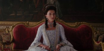 Movie still from “Queen Charlotte: A Bridgerton Story” (2023), directed by Tom Verica – A woman sitting on top of a couch wearing a dress; Medium shot, Low angle