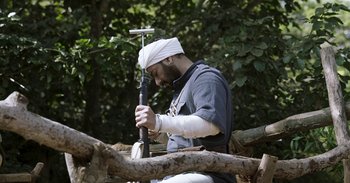 Movie still from “RRR” (2022), directed by S.S. Rajamouli – A man with a bandage on his head holding a stick; Medium shot, High angle