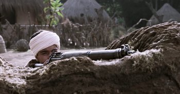 Movie still from “RRR” (2022), directed by S.S. Rajamouli – A man with a white bandage on his head is holding a rifle; Medium shot, High angle