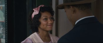 Movie still from “Race” (2016), directed by Stephen Hopkins – A young woman wearing a pink bow is smiling at a man; Close Up shot, Over the shoulder angle