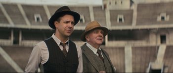 Movie still from “Race” (2016), directed by Stephen Hopkins – A couple of men standing next to each other wearing hats; Medium shot, Low angle