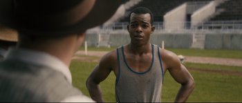 Movie still from “Race” (2016), directed by Stephen Hopkins – A man standing on a field looking at another man; Medium shot, Over the shoulder angle