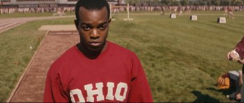 Movie still from “Race” (2016), directed by Stephen Hopkins – A man in a red shirt is standing in the grass; Close Up shot, Over the shoulder angle