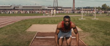 Movie still from “Race” (2016), directed by Stephen Hopkins – A man is crouched down on a track in front of a crowd; Medium shot, High angle