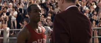 Movie still from “Race” (2016), directed by Stephen Hopkins – A man is being interviewed by an announcer; Close Up shot, Over the shoulder angle