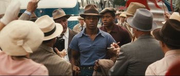 Movie still from “Race” (2016), directed by Stephen Hopkins – A group of men standing next to each other on the street; Medium shot, Over the shoulder angle