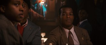 Movie still from “Race” (2016), directed by Stephen Hopkins – A man sitting at a table with a glass of wine in front of him; Close Up shot, Over the shoulder angle