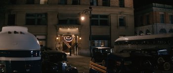 Movie still from “Race” (2016), directed by Stephen Hopkins – A man standing in front of a building at night; Extreme Wide shot, High angle