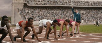Movie still from “Race” (2016), directed by Stephen Hopkins – A group of men on a track in a race; Wide shot, High angle
