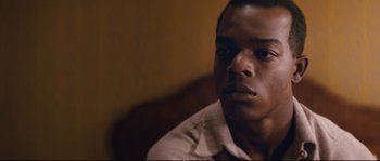 Movie still from “Race” (2016), directed by Stephen Hopkins – A man sitting in front of a wall looking at the camera; Close Up shot, Over the shoulder angle