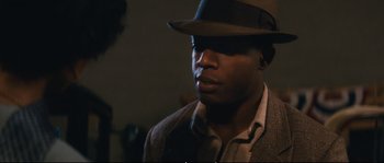 Movie still from “Race” (2016), directed by Stephen Hopkins – A man wearing a hat and a jacket; Close Up shot, Over the shoulder angle