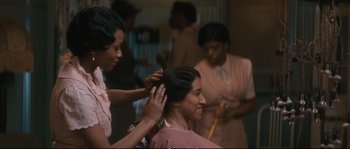 Movie still from “Race” (2016), directed by Stephen Hopkins – A woman getting her hair done by two other women; Medium shot, Over the shoulder angle