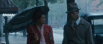 Movie still from “Race” (2016), directed by Stephen Hopkins – A woman holding an umbrella while standing next to a man; Medium shot, Low angle