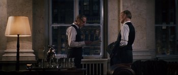 Movie still from “Race” (2016), directed by Stephen Hopkins – Two men standing next to each other in front of a window; Medium shot, Over the shoulder angle