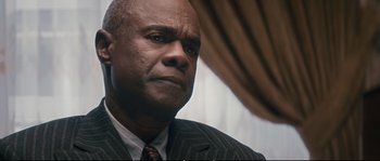 Movie still from “Race” (2016), directed by Stephen Hopkins – A person wearing a suit and tie; Close Up shot, Over the shoulder angle
