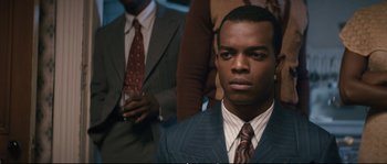 Movie still from “Race” (2016), directed by Stephen Hopkins – A man wearing a suit and tie in front of other men; Close Up shot, Over the shoulder angle