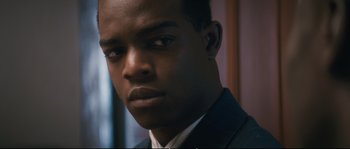 Movie still from “Race” (2016), directed by Stephen Hopkins – A person wearing a suit and ear buds; Close Up shot, Over the shoulder angle