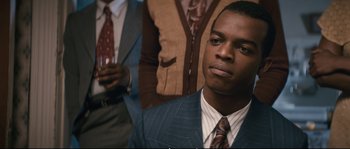 Movie still from “Race” (2016), directed by Stephen Hopkins – A man in a suit and tie looking at the camera; Close Up shot, Over the shoulder angle
