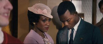 Movie still from “Race” (2016), directed by Stephen Hopkins – A man and a woman standing next to each other; Close Up shot, Over the shoulder angle