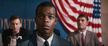 Movie still from “Race” (2016), directed by Stephen Hopkins – A man wearing a suit and tie looking at the camera; Close Up shot, Over the shoulder angle