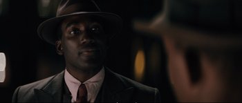 Movie still from “Race” (2016), directed by Stephen Hopkins – A man wearing a suit and a hat; Close Up shot, Over the shoulder angle