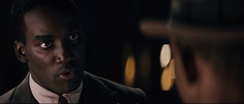 Movie still from “Race” (2016), directed by Stephen Hopkins – A person wearing a suit and tie; Close Up shot, Over the shoulder angle