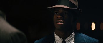 Movie still from “Race” (2016), directed by Stephen Hopkins – A man wearing a hat and a suit and tie; Close Up shot, Low angle