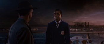 Movie still from “Race” (2016), directed by Stephen Hopkins – A man in a suit and tie standing next to another man in a suit and tie; Medium shot, Over the shoulder angle