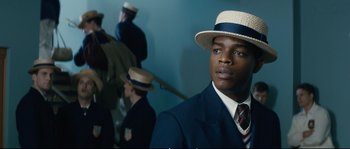 Movie still from “Race” (2016), directed by Stephen Hopkins – A man in a suit and straw hat in front of other men; Close Up shot, Over the shoulder angle