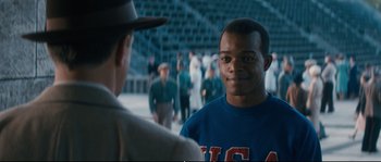 Movie still from “Race” (2016), directed by Stephen Hopkins – A man in a hat is shaking hands with another man in a baseball uniform; Medium shot, Over the shoulder angle