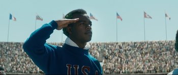 Movie still from “Race” (2016), directed by Stephen Hopkins – A young man saluting in front of an audience; Medium shot, Low angle