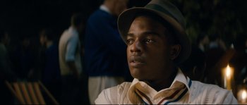 Movie still from “Race” (2016), directed by Stephen Hopkins – A young man wearing a hat and a neck tie; Close Up shot, Over the shoulder angle