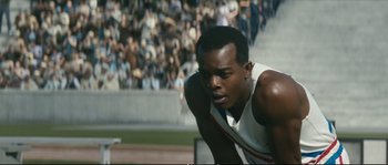 Movie still from “Race” (2016), directed by Stephen Hopkins – A man in a white shirt is crouching on a track; Close Up shot, High angle
