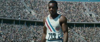 Movie still from “Race” (2016), directed by Stephen Hopkins – A man is standing in front of a crowd of people; Medium shot, High angle