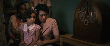 Movie still from “Race” (2016), directed by Stephen Hopkins – A woman sitting next to a little girl in front of a clock; Medium shot, Over the shoulder angle