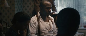 Movie still from “Race” (2016), directed by Stephen Hopkins – A man in a white dress shirt and brown suspenders; Medium shot, Over the shoulder angle