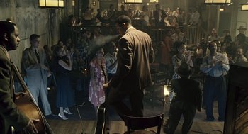 Movie still from “Ray” (2004), directed by Taylor Hackford – A man in a brown suit is holding a guitar in front of a group of people; Wide shot, High angle