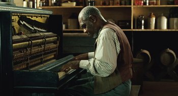 Movie still from “Ray” (2004), directed by Taylor Hackford – An older man playing the piano in a room; Medium shot, High angle