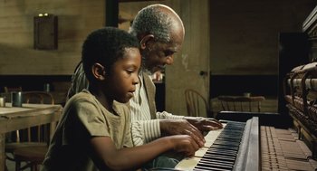 An older man teaching a young boy how to play the piano