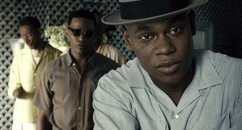 Movie still from “Ray” (2004), directed by Taylor Hackford – A man in a hat and sunglasses is looking at the camera; Close Up shot, Over the shoulder angle