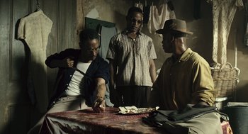 Movie still from “Ray” (2004), directed by Taylor Hackford – A group of men standing around a table with papers; Medium shot, High angle