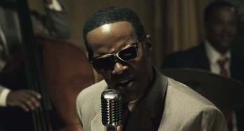 Movie still from “Ray” (2004), directed by Taylor Hackford – A man in a suit and sunglasses is holding a microphone; Close Up shot, Low angle