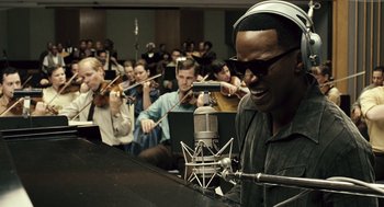 Movie still from “Ray” (2004), directed by Taylor Hackford – A group of people in a room with a microphone; Close Up shot, Over the shoulder angle