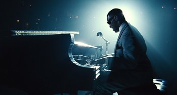 Movie still from “Ray” (2004), directed by Taylor Hackford – A man in a suit and sunglasses playing a piano; Wide shot, High angle