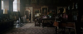 Movie still from “Rebecca” (2020), directed by Ben Wheatley – A woman standing in front of a table in a living room; Extreme Wide shot, Low angle
