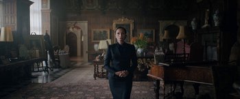 Movie still from “Rebecca” (2020), directed by Ben Wheatley – A woman standing in a living room wearing a suit; Medium shot, Low angle