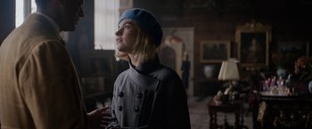 Movie still from “Rebecca” (2020), directed by Ben Wheatley – A woman wearing a blue hat standing in a living room; Medium shot, Over the shoulder angle